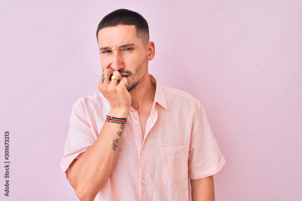 Young handsome man wearing pink shirt standing over isolated background looking stressed and nervous with hands on mouth biting nails. Anxiety problem. Young handsome man wearing pink shirt standing over isolated background looking stressed and nervous with hands on mouth biting nails. Anxiety problem.