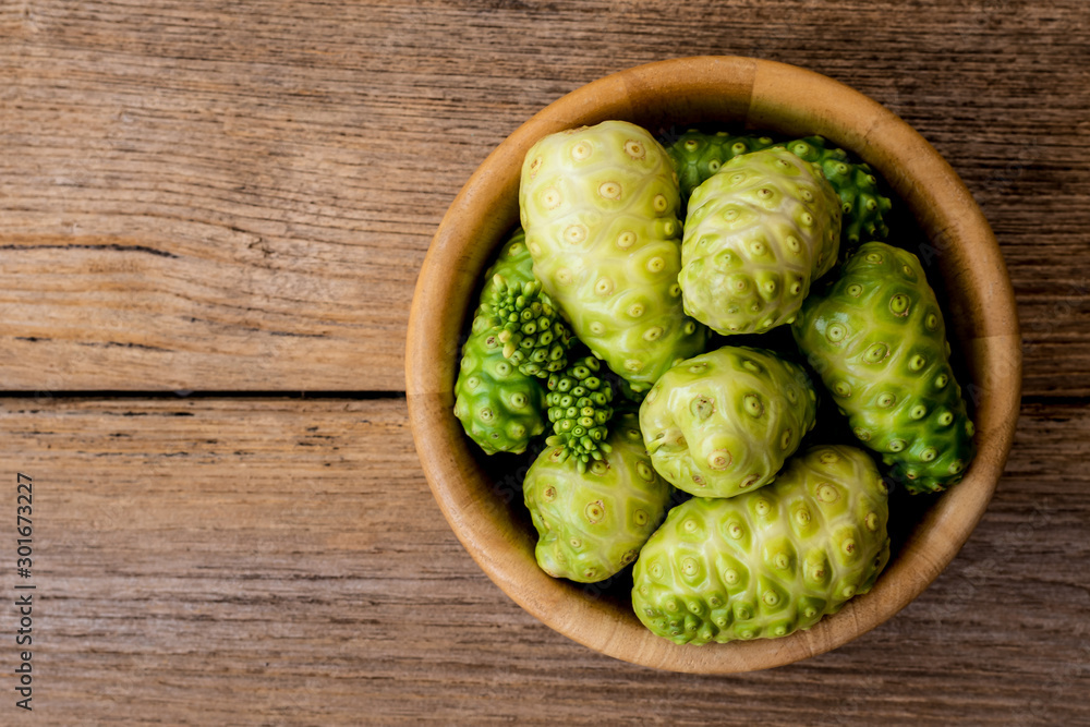 Fresh raw and ripe Morinda citrifolia or Noni fruit and sliced with seeds in wooden bowl isolated on wood background. Fresh raw and ripe Morinda citrifolia or Noni fruit and sliced with seeds in wooden bowl isolated on wood background.
