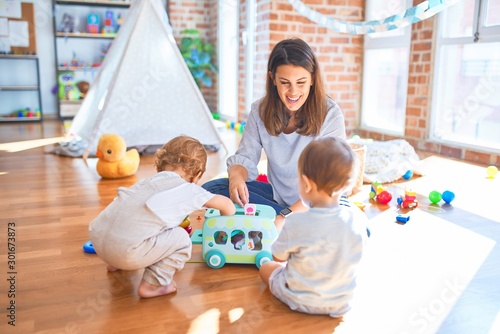 Beautiful teacher and toddlers playing around lots of toys at kindergarten photo