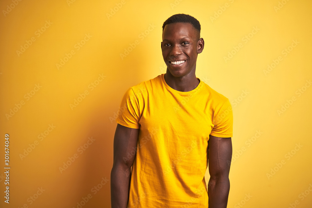 Young african american man wearing casual t-shirt standing over isolated yellow background looking away to side with smile on face, natural expression. Laughing confident. Young african american man wearing casual t-shirt standing over isolated yellow background looking away to side with smile on face, natural expression. Laughing confident.