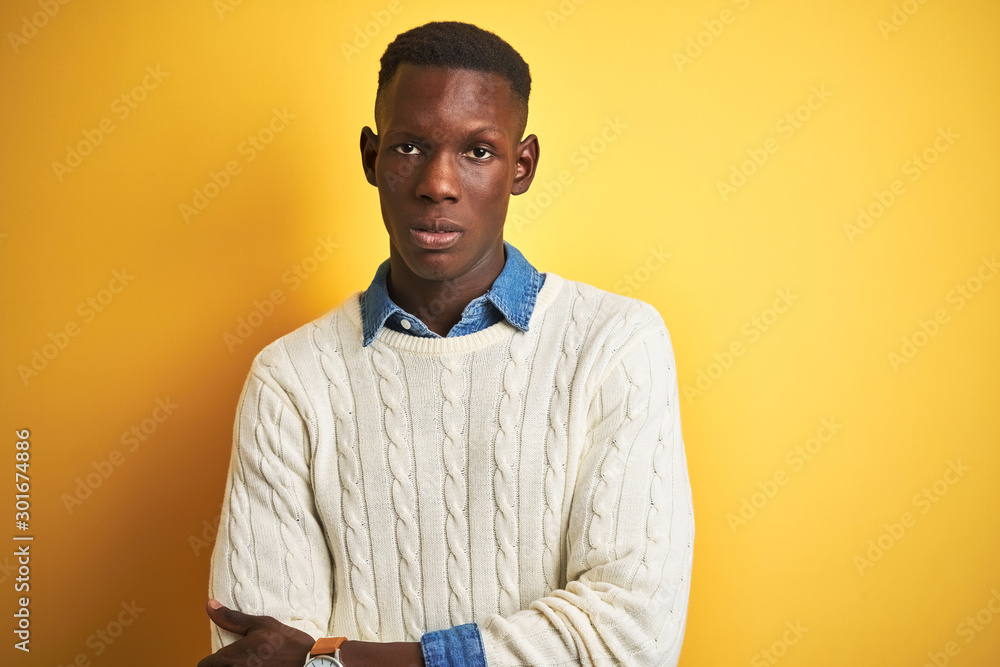 Obraz premium African american man wearing denim shirt and white sweater over isolated yellow background skeptic and nervous, disapproving expression on face with crossed arms. Negative person.