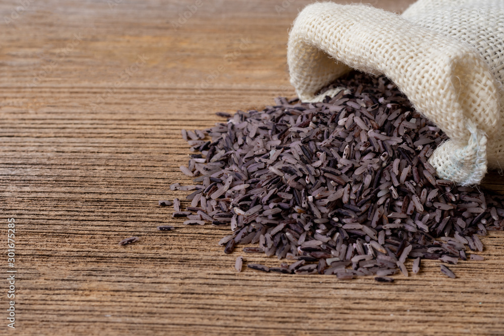 Black jasmine rice( Riceberry, red cargo rice ) in sack bag isolated on old rustic wooden table background. Healthy, vegetarian food and diet concept. Space for text and content. Vintage style. Black jasmine rice( Riceberry, red cargo rice ) in sack bag isolated on old rustic wooden table background. Healthy, vegetarian food and diet concept. Space for text and content. Vintage style.