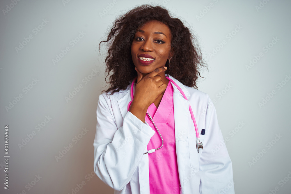 African american doctor woman wearing  pink stethoscope over isolated white background looking confident at the camera smiling with crossed arms and hand raised on chin. Thinking positive.