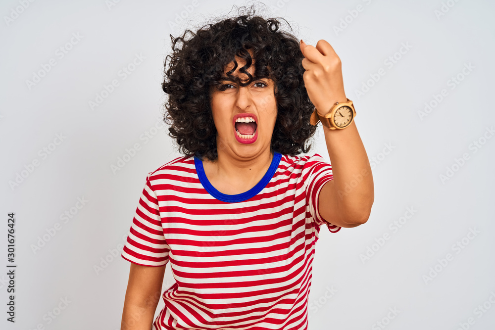 Young arab woman with curly hair wearing striped t-shirt over isolated white background angry and mad raising fist frustrated and furious while shouting with anger. Rage and aggressive concept. Young arab woman with curly hair wearing striped t-shirt over isolated white background angry and mad raising fist frustrated and furious while shouting with anger. Rage and aggressive concept.