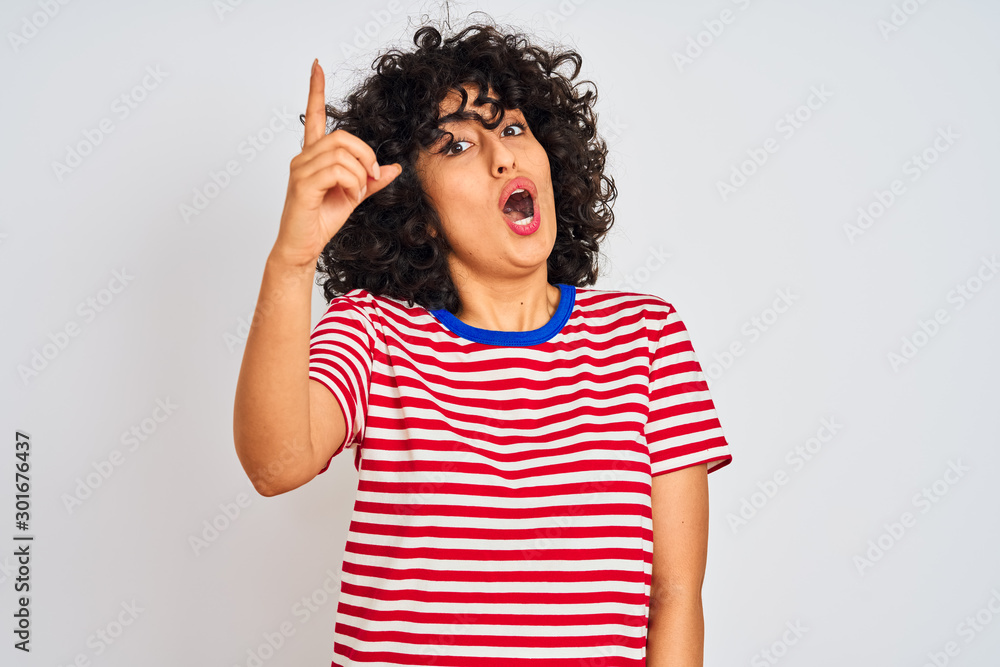 Young arab woman with curly hair wearing striped t-shirt over isolated white background pointing finger up with successful idea. Exited and happy. Number one. Young arab woman with curly hair wearing striped t-shirt over isolated white background pointing finger up with successful idea. Exited and happy. Number one.