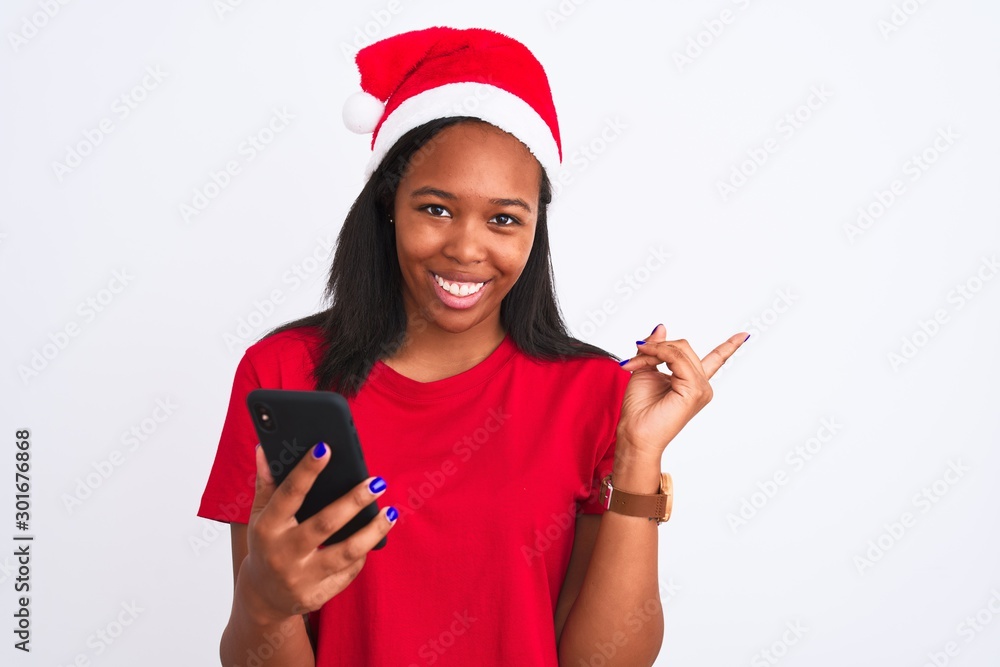 Young african american woman wearing christmas hat and using smartphone very happy pointing with hand and finger to the side Young african american woman wearing christmas hat and using smartphone very happy pointing with hand and finger to the side
