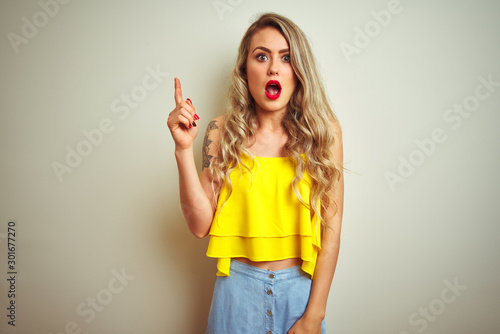 Young beautiful woman wearing yellow t-shirt standing over white isolated background pointing finger up with successful idea. Exited and happy. Number one.