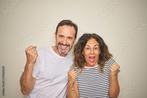 Beautiful middle age couple together standing over isolated white background celebrating surprised and amazed for success with arms raised and open eyes. Winner concept.