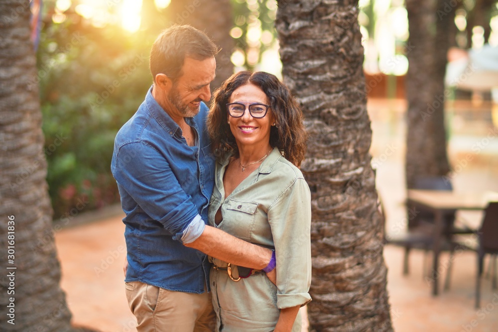 Naklejka premium Middle age beautiful couple smiling happy and confident at town park. Standing with smile on face and hugging