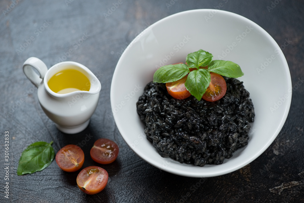 Risotto with squid-ink served in a white bowl over dark brown stone surface, studio shot Risotto with squid-ink served in a white bowl over dark brown stone surface, studio shot