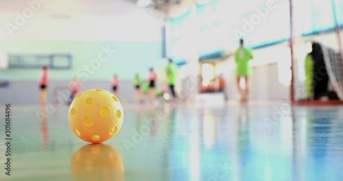 Floorball match of small floorball players. Children play floorball match in indoor hall. Intentionally focused on the ball in the foreground. Players in the background intentionally out of focus.