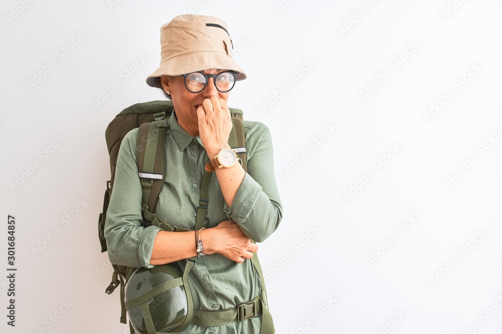 Middle age hiker woman wearing backpack canteen hat glasses over isolated white background looking stressed and nervous with hands on mouth biting nails. Anxiety problem. Middle age hiker woman wearing backpack canteen hat glasses over isolated white background looking stressed and nervous with hands on mouth biting nails. Anxiety problem.