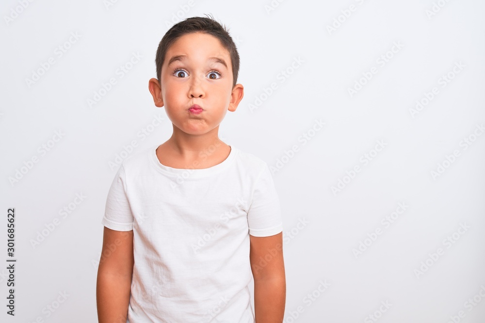 Beautiful kid boy wearing casual t-shirt standing over isolated white background puffing cheeks with funny face. Mouth inflated with air, crazy expression. Beautiful kid boy wearing casual t-shirt standing over isolated white background puffing cheeks with funny face. Mouth inflated with air, crazy expression.