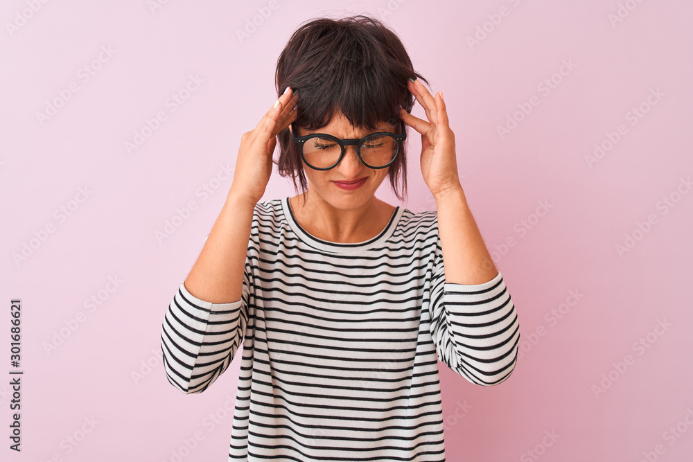 Young beautiful woman wearing striped t-shirt and glasses over isolated pink background with hand on head for pain in head because stress. Suffering migraine. Young beautiful woman wearing striped t-shirt and glasses over isolated pink background with hand on head for pain in head because stress. Suffering migraine.