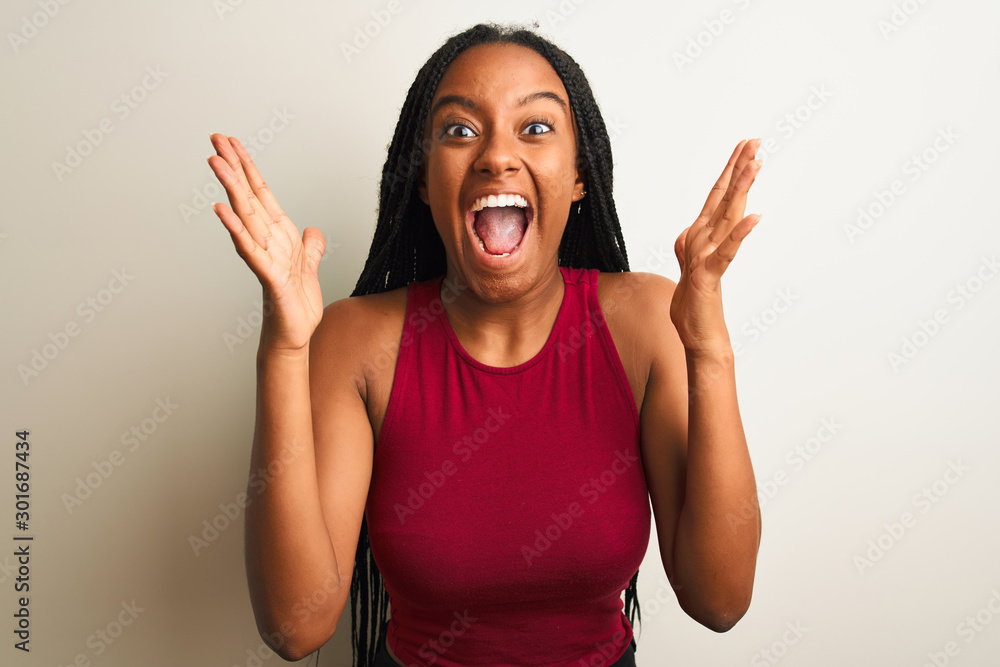African american woman wearing red casual t-shirt standing over isolated white background celebrating crazy and amazed for success with arms raised and open eyes screaming excited. Winner concept African american woman wearing red casual t-shirt standing over isolated white background celebrating crazy and amazed for success with arms raised and open eyes screaming excited. Winner concept