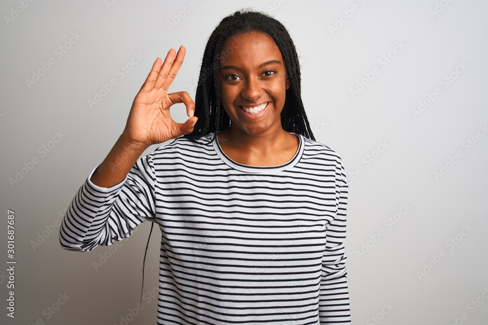 Young african american woman wearing striped t-shirt standing over isolated white background smiling positive doing ok sign with hand and fingers. Successful expression. Young african american woman wearing striped t-shirt standing over isolated white background smiling positive doing ok sign with hand and fingers. Successful expression.