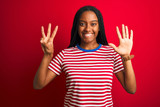 Young african american woman wearing striped t-shirt standing over isolated red background showing and pointing up with fingers number eight while smiling confident and happy.