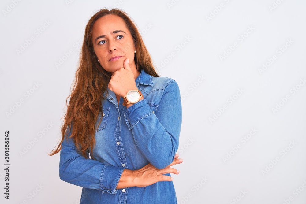 Middle age mature woman wearing denim jacket standing over white isolated background looking confident at the camera with smile with crossed arms and hand raised on chin. Thinking positive. Middle age mature woman wearing denim jacket standing over white isolated background looking confident at the camera with smile with crossed arms and hand raised on chin. Thinking positive.