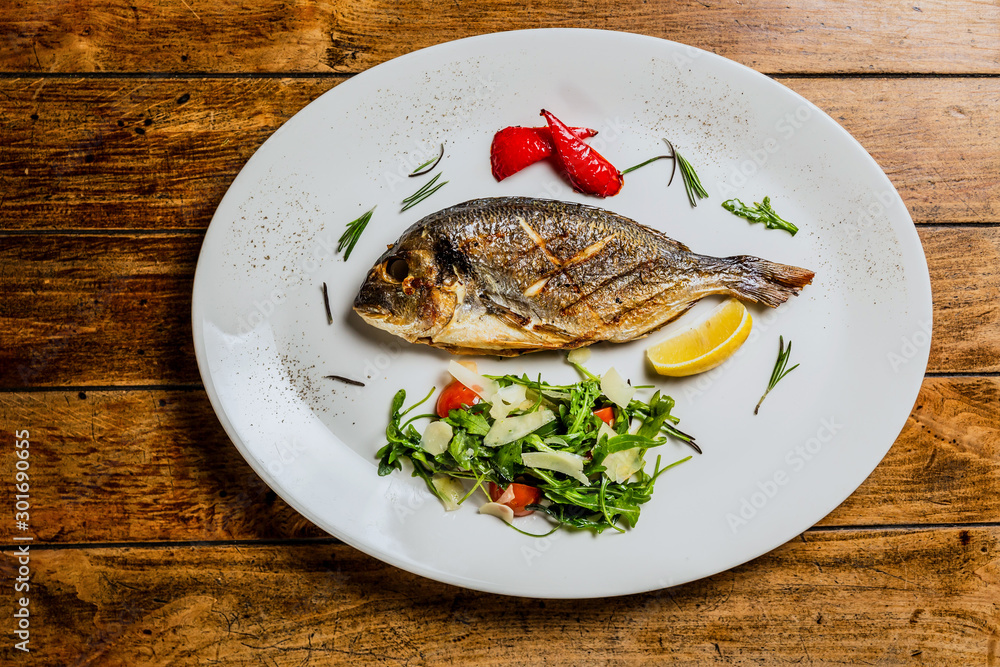 Grilled fish with arugula salad on white plate. Top view landscape image Grilled fish with arugula salad on white plate. Top view landscape image