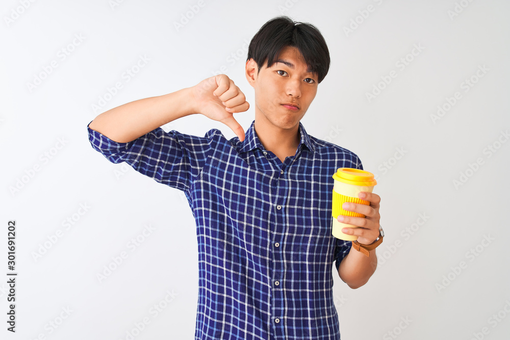 Young chinese man drinking take away coffee standing over isolated white background with angry face, negative sign showing dislike with thumbs down, rejection concept Young chinese man drinking take away coffee standing over isolated white background with angry face, negative sign showing dislike with thumbs down, rejection concept