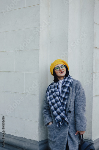 Attractive young girl in glasses in coat and yellow Beret on a simple light background © pressahotkey