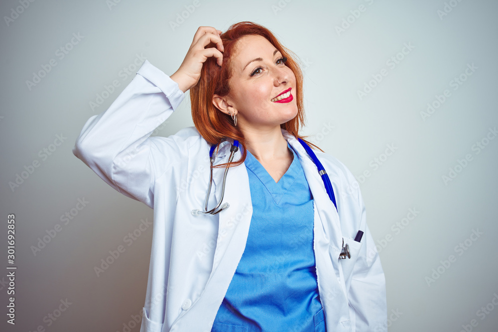 Young redhead doctor woman using stethoscope over white isolated background smiling confident touching hair with hand up gesture, posing attractive and fashionable Young redhead doctor woman using stethoscope over white isolated background smiling confident touching hair with hand up gesture, posing attractive and fashionable