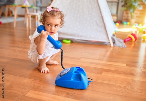 Beautiful caucasian infant playing with toys at colorful playroom. Happy and playful calling with vitange telephone at kindergarten.