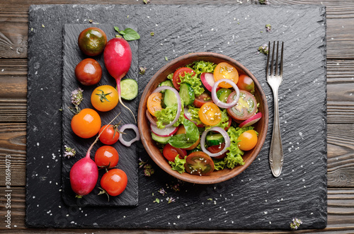 Top view at vegetable salad of lettuce, cherry tomatoes, radish, cucumber, onion and basil on slate stone tray