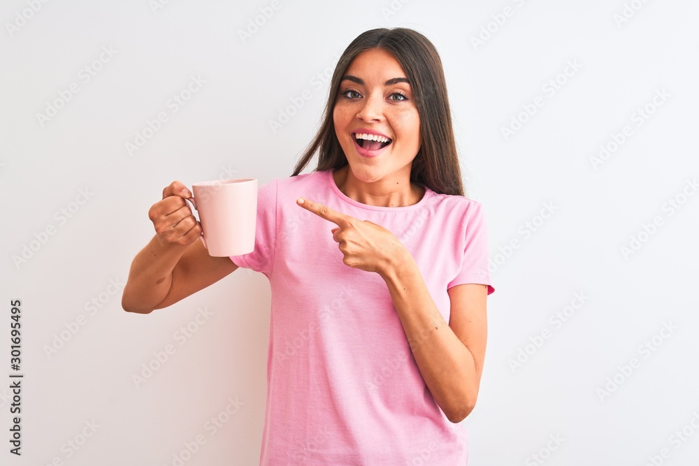 Young beautiful woman drinking pink cup of coffee standing over isolated white background very happy pointing with hand and finger Young beautiful woman drinking pink cup of coffee standing over isolated white background very happy pointing with hand and finger