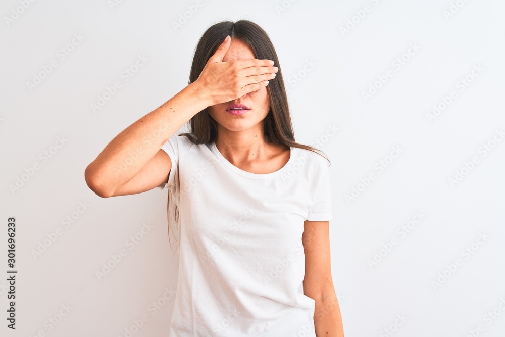 Young beautiful woman wearing casual t-shirt standing over isolated white background covering eyes with hand, looking serious and sad. Sightless, hiding and rejection concept Young beautiful woman wearing casual t-shirt standing over isolated white background covering eyes with hand, looking serious and sad. Sightless, hiding and rejection concept