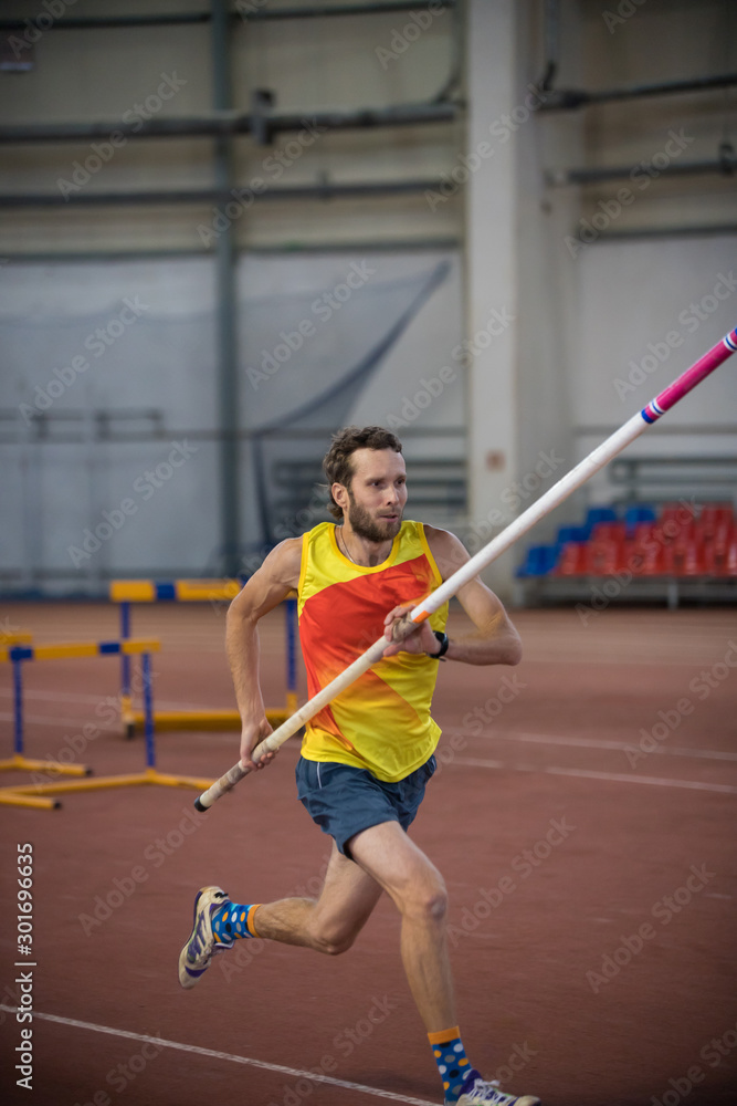 Pole vaulting indoors - a man running on the track with a pole in the stadium