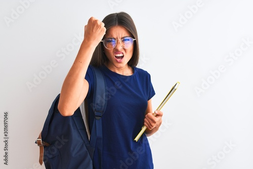 Young student woman wearing backpack glasses holding book over isolated white background annoyed and frustrated shouting with anger, crazy and yelling with raised hand, anger concept