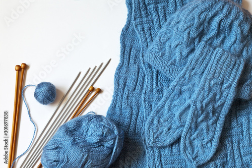 Needlework and craft. Hand-knitted blue mittens, scarf and warm hat for winter. Balls of wool yarn and set of metal and wooden needles on white background. Top view, copy space, close-up, flat lay