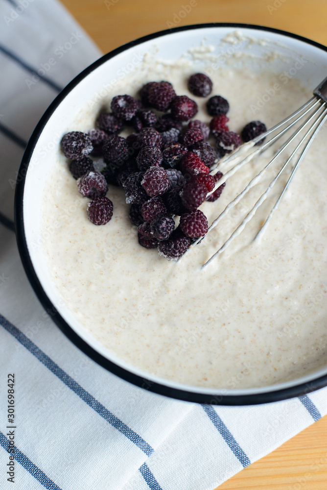 black raspberry in white metal bowl with batter and whisk on wooden table, cooking homemade oladyi or pancakes with wholegrain flour and blackberry, top view of vertical life style stock photo image