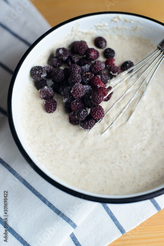 Obraz na płótnie black raspberry in white metal bowl with batter and whisk on wooden table, cooking homemade oladyi or pancakes with wholegrain flour and blackberry, top view of vertical life style stock photo image w salonie