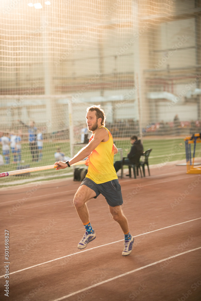 Pole vaulting in the sports stadium - an athletic man running on the track