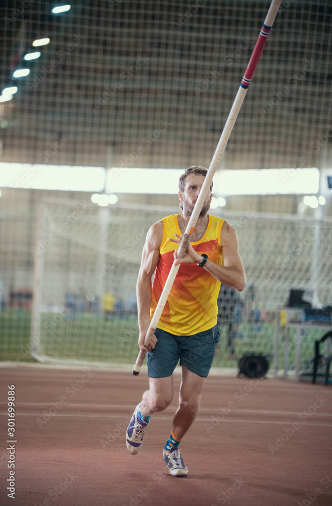 Pole vaulting in the sports stadium - an athletic man in yellow shirt running on the track