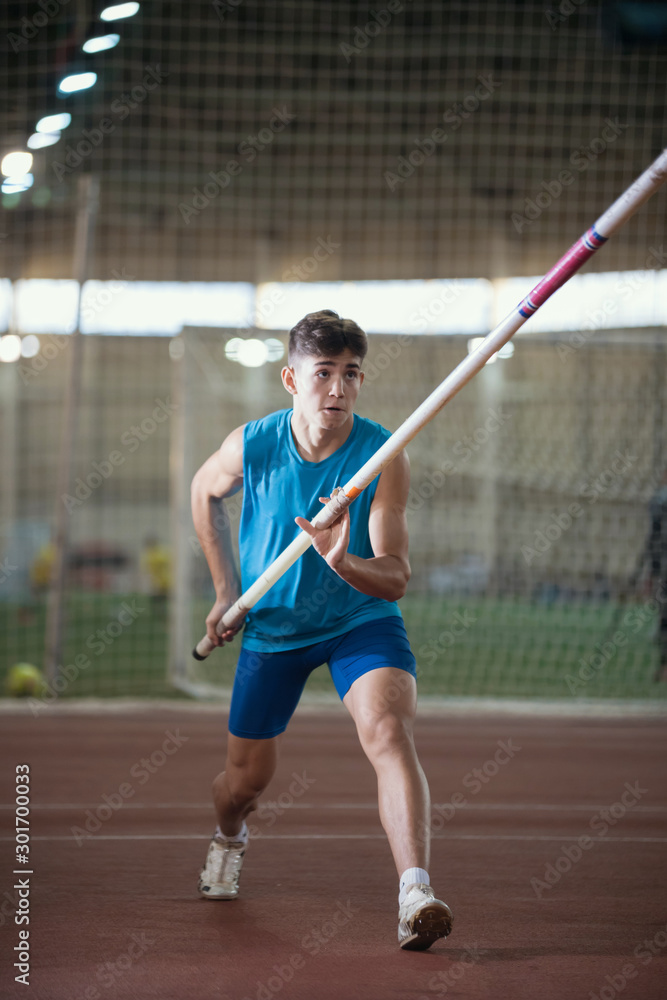 Pole vault training in the sports stadium - young man running on the track holding a pole