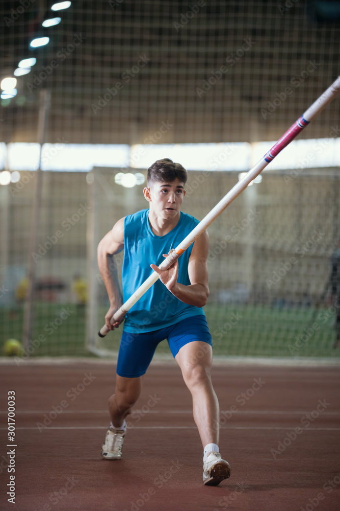 Pole vault training in the sports stadium - young man running on the track holding a pole Pole vault training in the sports stadium - young man running on the track holding a pole