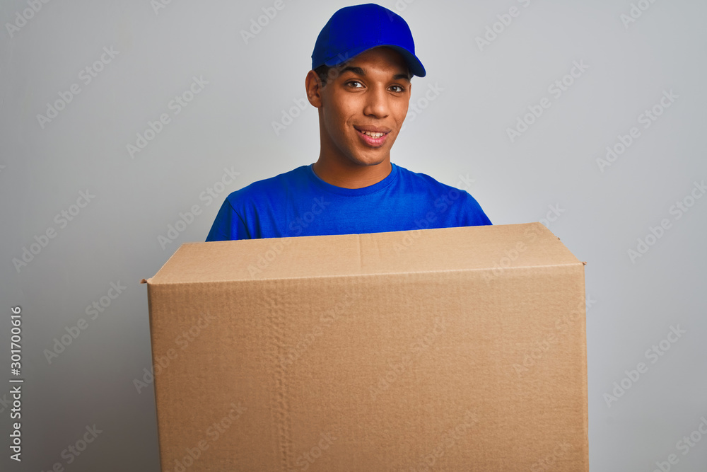Young handsome arab delivery man holding a box standing over isolated white background with a happy face standing and smiling with a confident smile showing teeth Young handsome arab delivery man holding a box standing over isolated white background with a happy face standing and smiling with a confident smile showing teeth