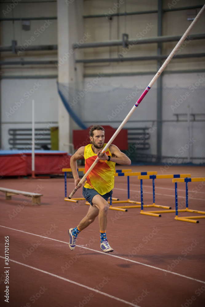 Pole vaulting - man in yellow shirt is running with a long pole in hands