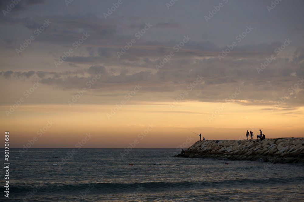 Fishermen in the evening on a sunset background fish in the calm sea. Amazing warm calm evening on the seashore during a wonderful summer vacation at the seaside resort.