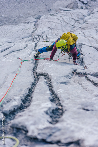 A climber climbing on a big rock wall. A mountaineer ascending a climbing route. Limestone climbing in the alps. Adventure extreme sport activity. Multi pitch climbing in huge alpine wall.