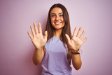 Young beautiful woman wearing casual t-shirt standing over isolated pink background showing and pointing up with fingers number ten while smiling confident and happy.
