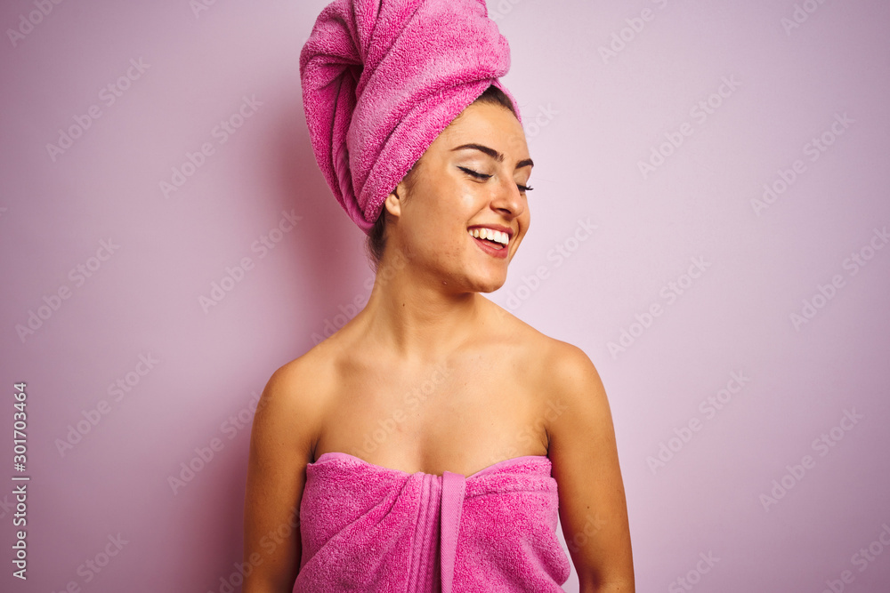 Young beautiful woman wearing towel after shower over isolated pink background looking away to side with smile on face, natural expression. Laughing confident. Young beautiful woman wearing towel after shower over isolated pink background looking away to side with smile on face, natural expression. Laughing confident.