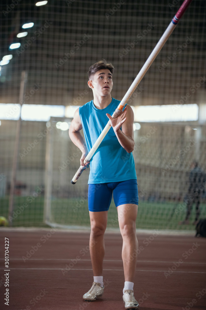 Pole vaulting - young guy in a blue suit is rising in hands a pole