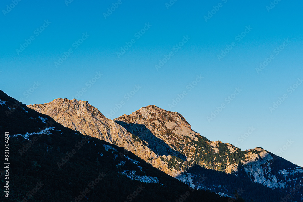 Beautiful sunset view of a mountain alpine landscape of Totes Gebirge, Austria. High alpine peaks in yellow and orange evening light. Rocky summit and rock walls of alpine peaks. Blue sky.