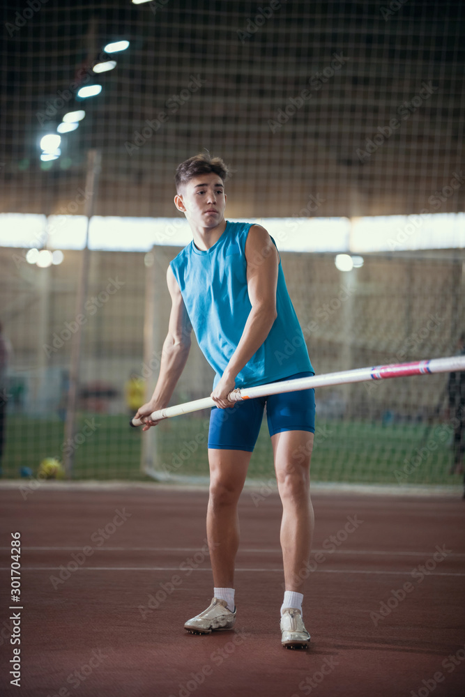 Pole vaulting - young guy in a blue suit is standing with a pole in hands