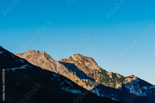 Beautiful sunset view of a mountain alpine landscape of Totes Gebirge  Austria. High alpine peaks in yellow and orange evening light. Rocky summit and rock walls of alpine peaks. Blue sky.
