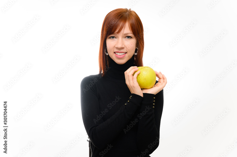Healthy food concept. Portrait of a pretty red-haired student girl with long smooth hair on a white background in a black sweater with an apple in her hands. Talking, showing emotions, smiling. Healthy food concept. Portrait of a pretty red-haired student girl with long smooth hair on a white background in a black sweater with an apple in her hands. Talking, showing emotions, smiling.